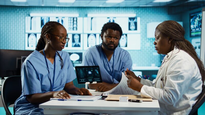 Team of male and female african american medical staff discussing diagnostic results with a medic expert in a modern cabinet. Advanced technology and healthcare services at clinic. Camera B.