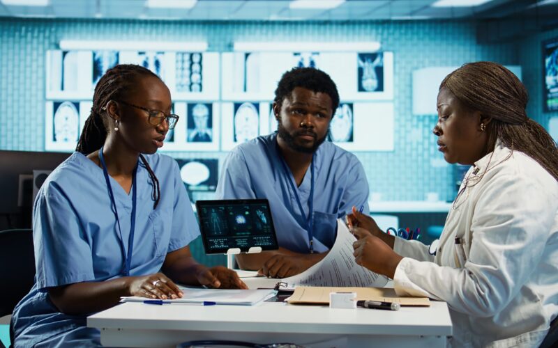 Team of male and female african american medical staff discussing diagnostic results with a medic expert in a modern cabinet. Advanced technology and healthcare services at clinic. Camera B.