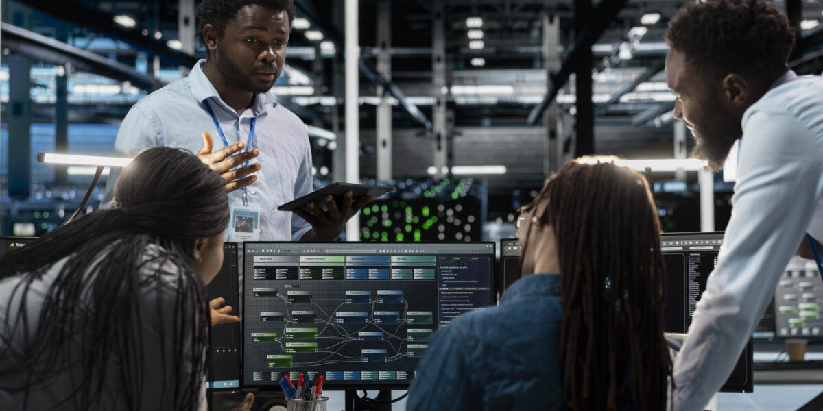 Engineers doing brainstorming, programming in server farm housing infrastructure storing datasets. Teamworking colleagues run code on PC to repair data center racks doing computational operations